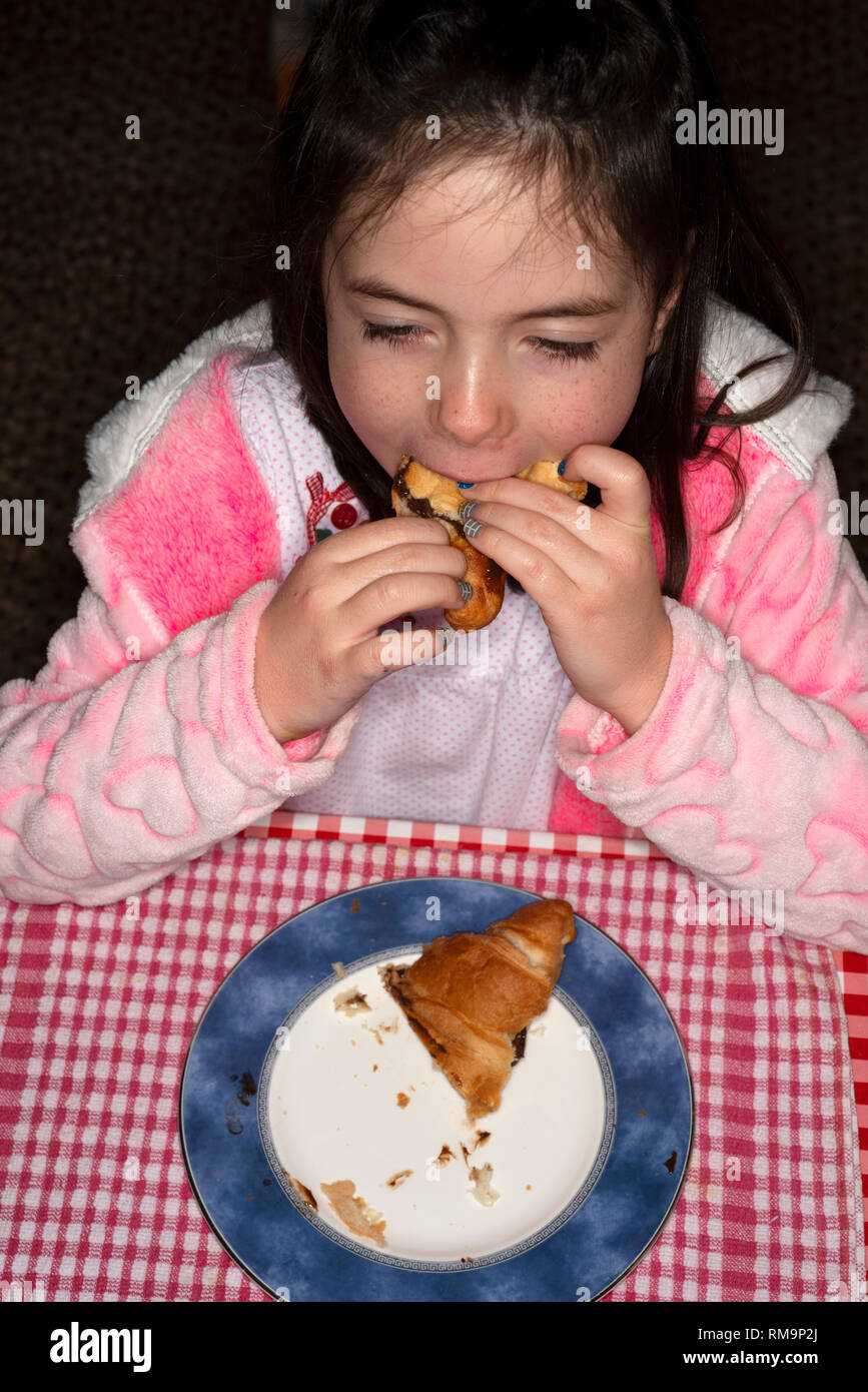 Young girl eating chocolate filled croissant for breakfast hires stock