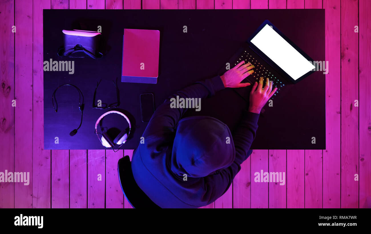 Cybercrime, hacking and technology concept - male hacker in dark room writing code or using computer virus program for cyber attack. White Display. Stock Photo