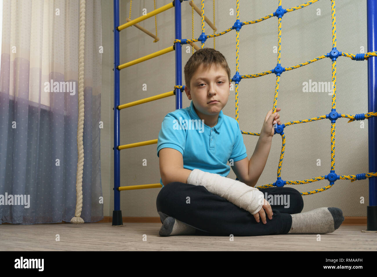 Sad child with a broken arm in the home environment . The cast on the hand of a little boy. Stock Photo