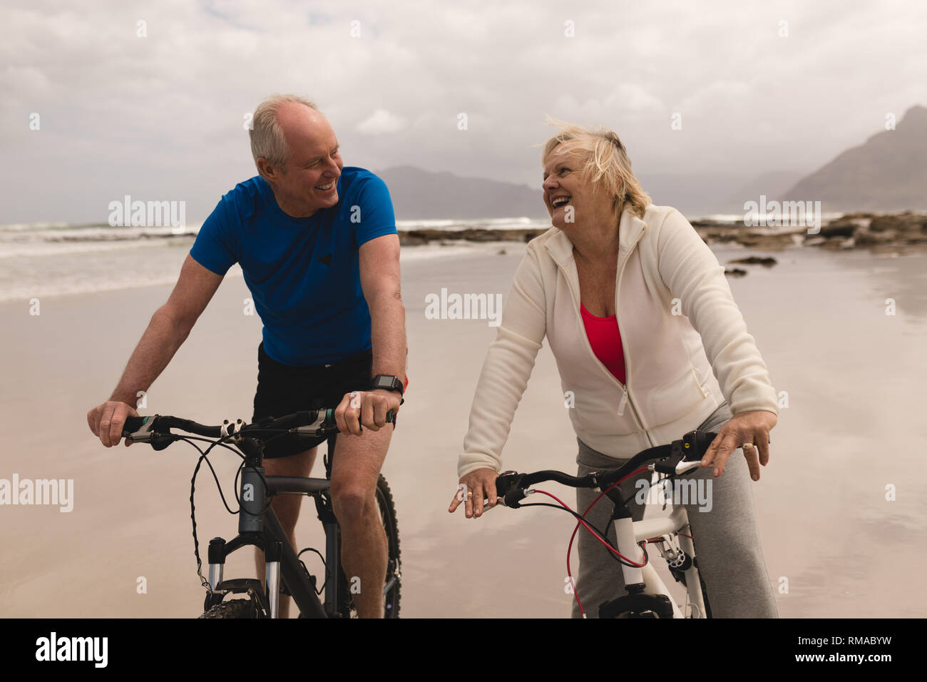 Senior couple riding a bicycle in a good mood on the beach Stock Photo