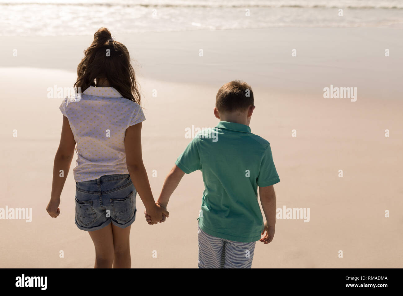 Siblings holding hands and walking on beach Stock Photo - Alamy