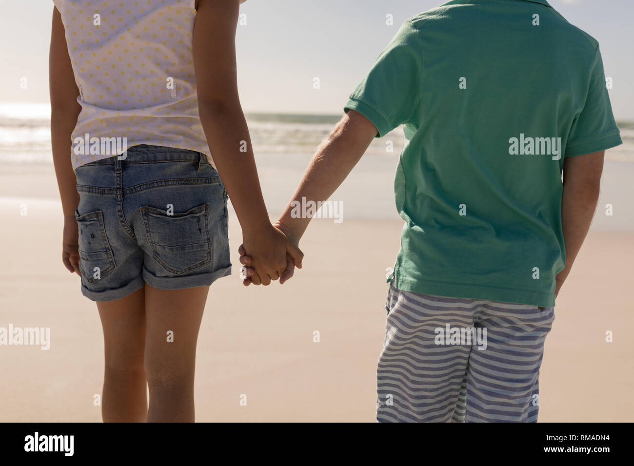 Siblings holding hands and standing on beach Stock Photo - Alamy