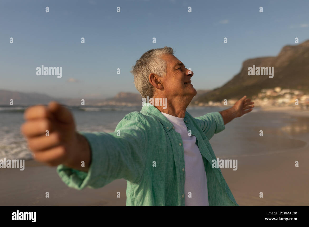 Senior man standing with arms outstretched on the beach Stock Photo
