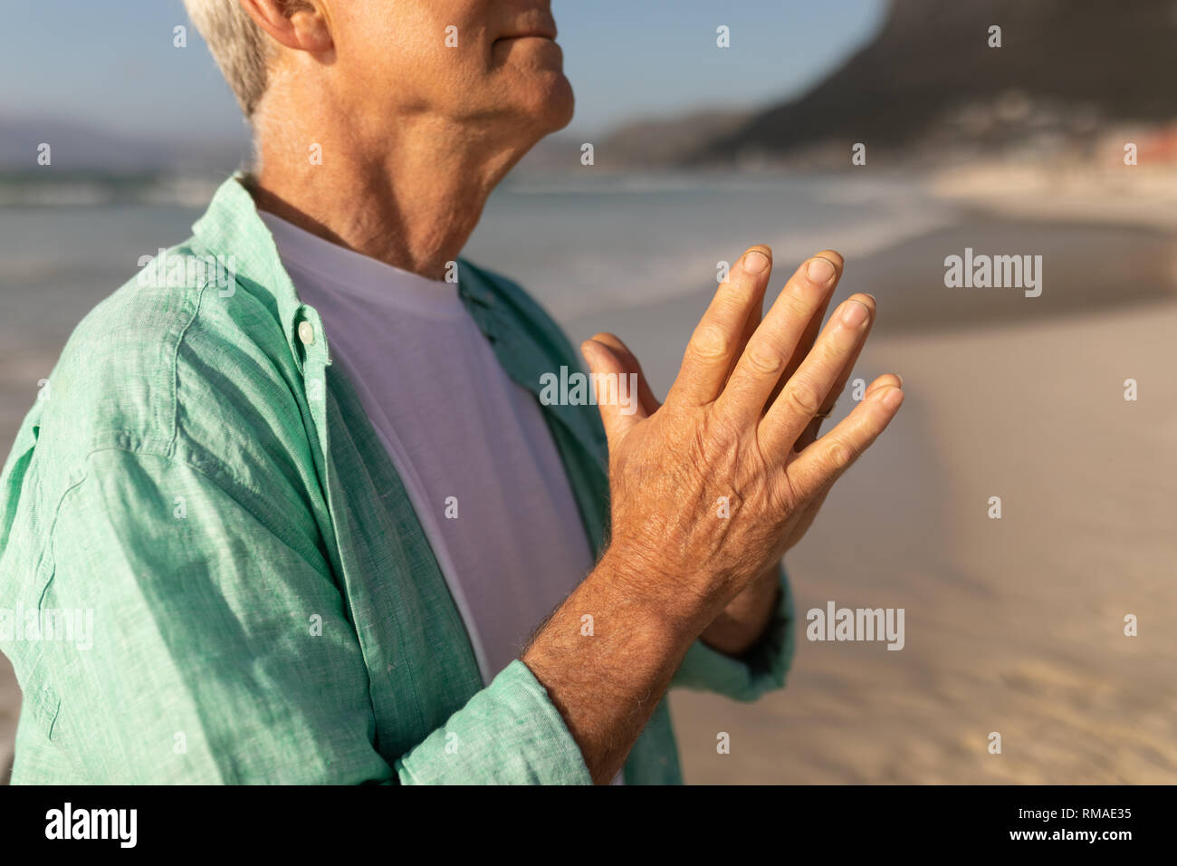 Senior man praying with eyes closed on the beach Stock Photo