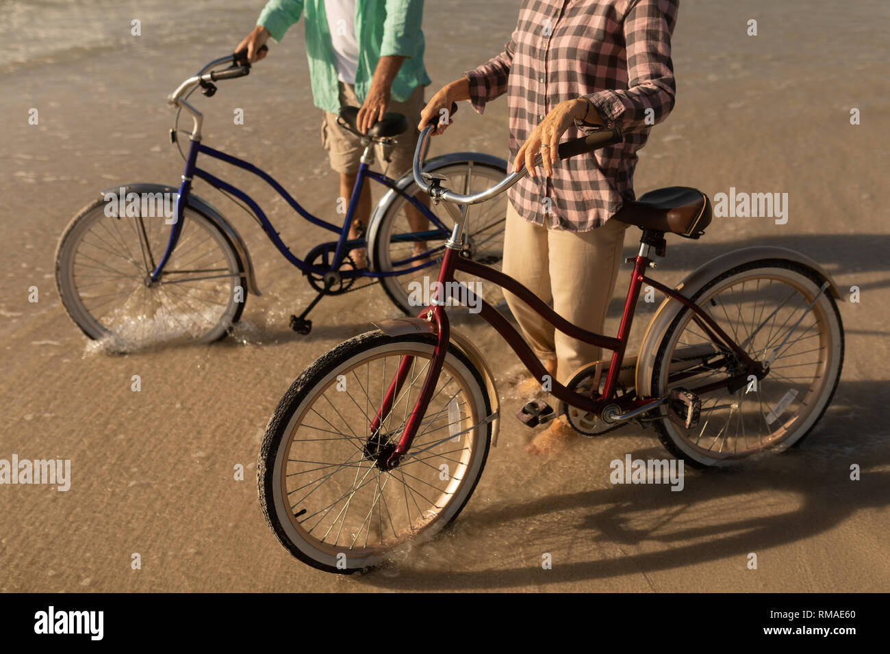 Senior couple standing with bicycle on the beach Stock Photo