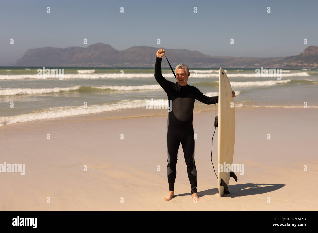 Side view of senior male surfer standing with surfboard on the beach Stock Photo
