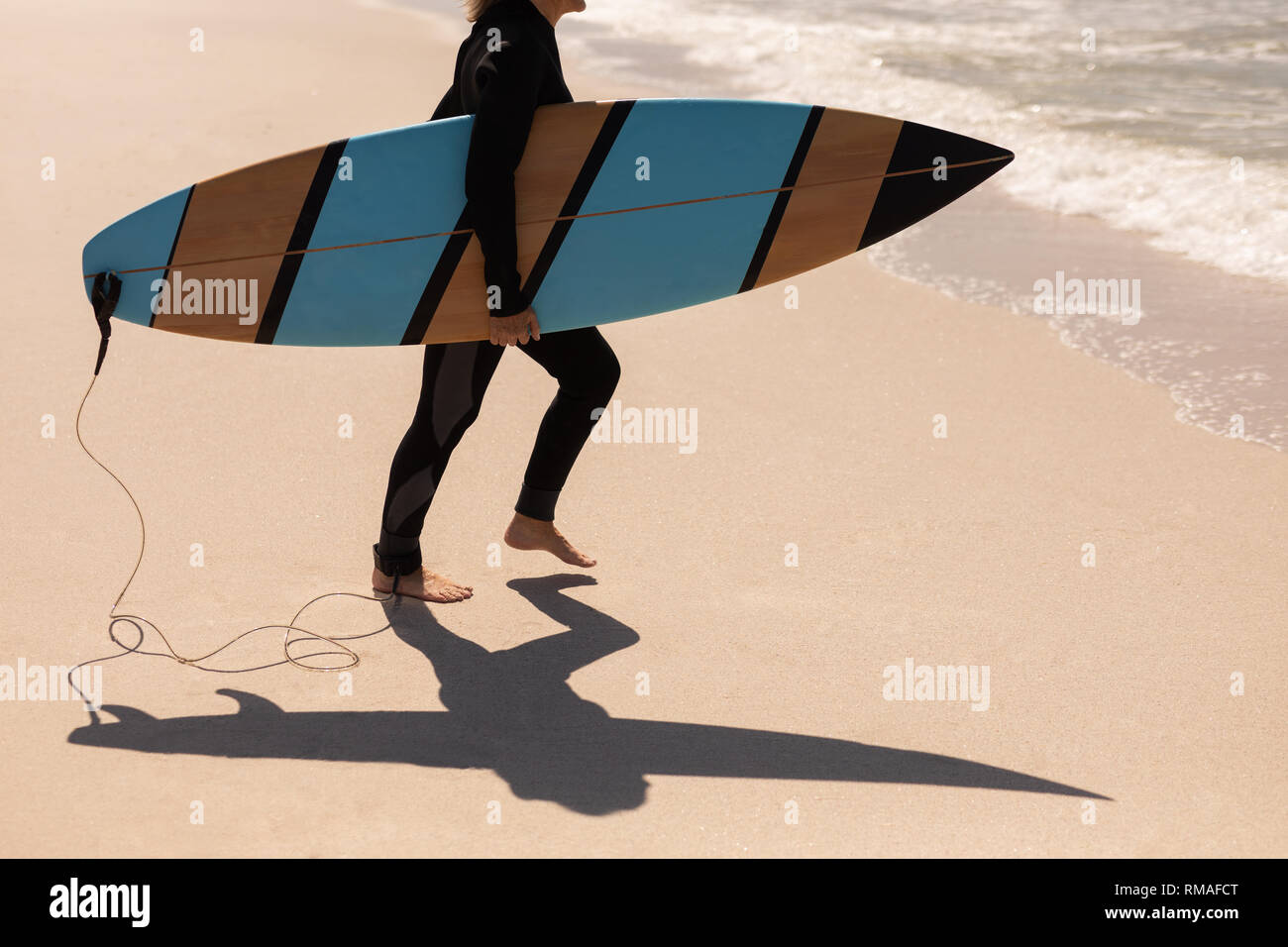 Low section of senior female surfer walking with surfboard on the beach