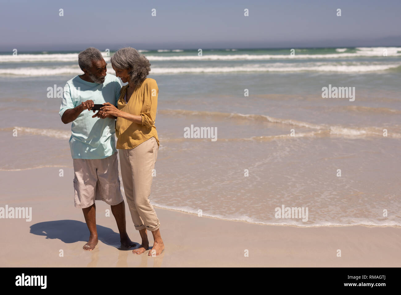 Senior couple reviewing photos on mobile phone on beach Stock Photo