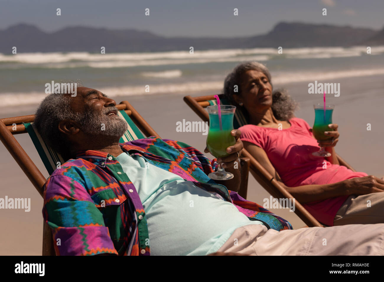 Senior couple relaxing on sun lounger and drinking cocktail on beach ...