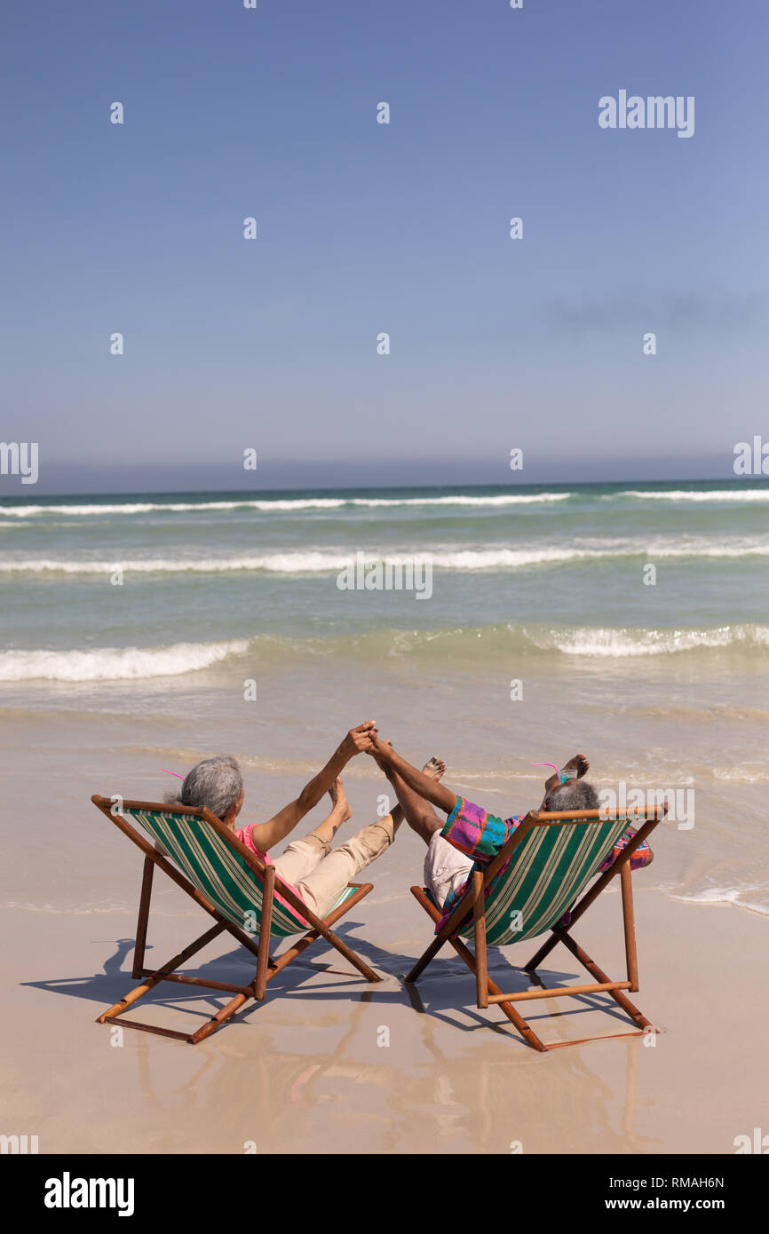 Senior couple relaxing on sun lounger and holding hands on beach Stock ...