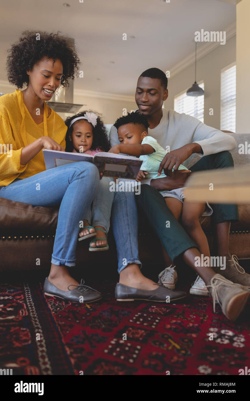 Happy African American parents with their cute children reading storybook on the sofa Stock Photo