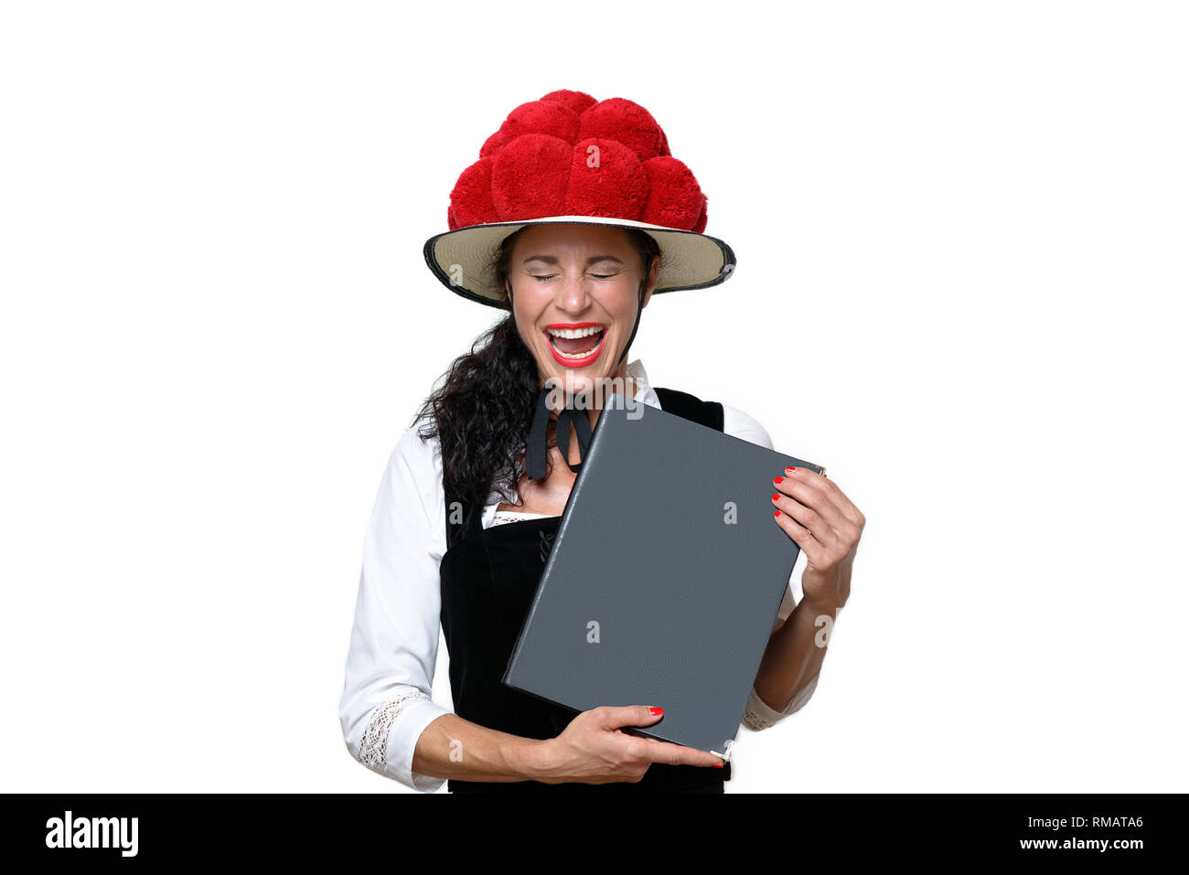 Candid portrait of a laughing attractive young Black Forest waitress holding a menu dressed in traditional clothes with a Bollenhut decorated with red Stock Photo