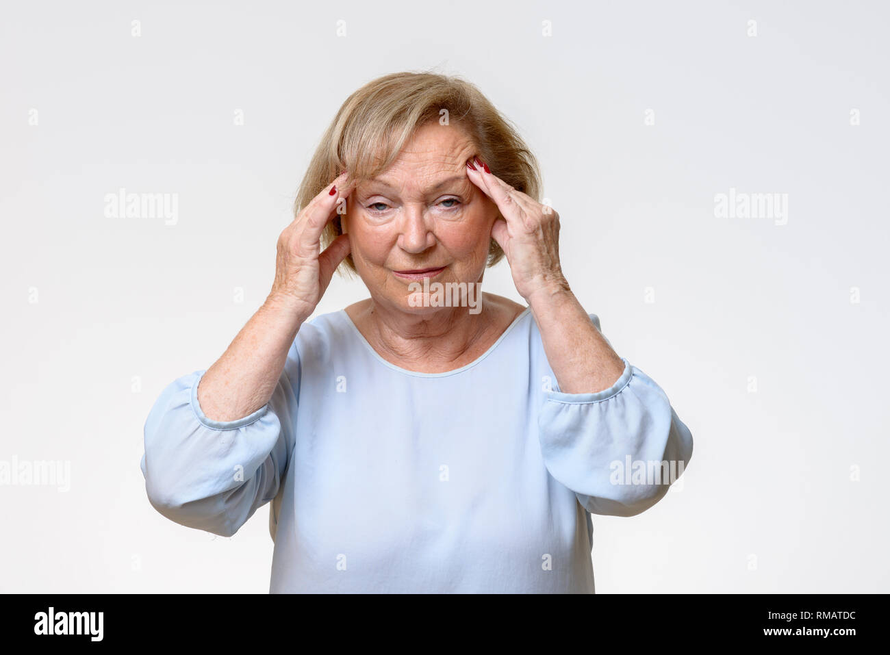 Senior woman suffering from a severe headache rubbing her temples with her fingers with an expression of pain on her face Stock Photo