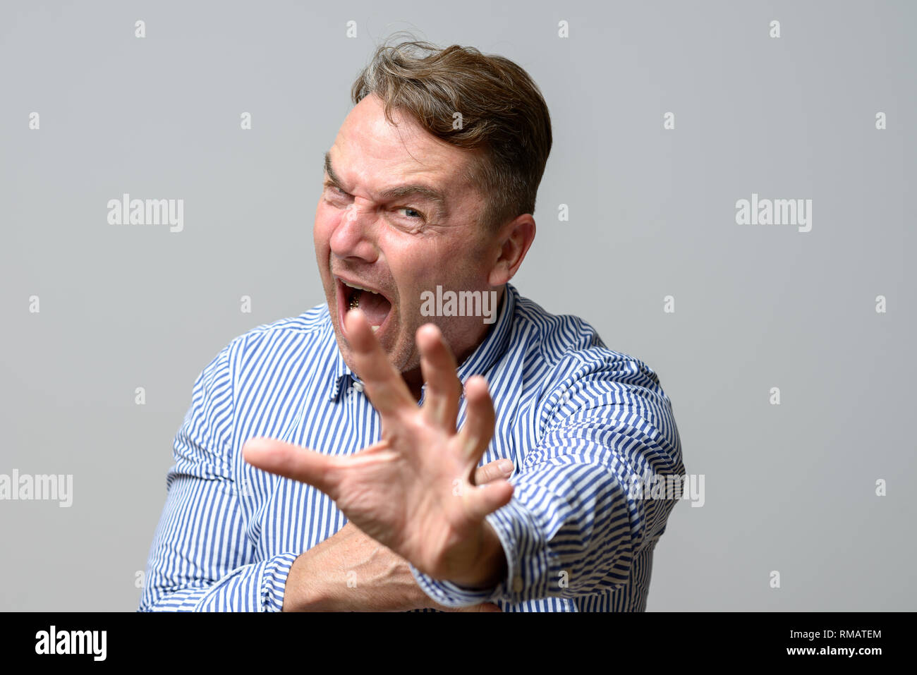 Middle aged man screaming at the camera with his hand outstretched as though in self defence, upper body over grey Stock Photo