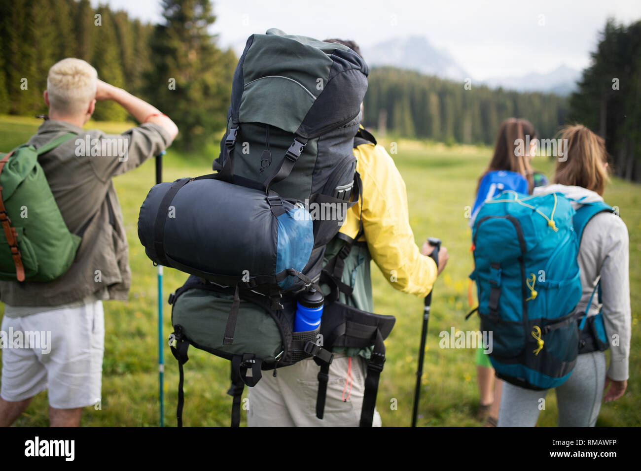Group of hikers with backpacks and sticks walking on mountain. Friends making an excursion Stock Photo