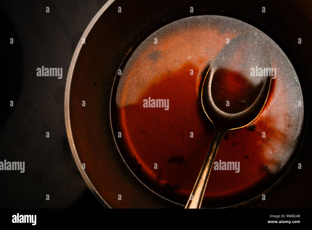 view into the pot with a spoon while cooking a morel sauce of beef stock and port wine, dark background with copy space, from above, selected focus Stock Photo
