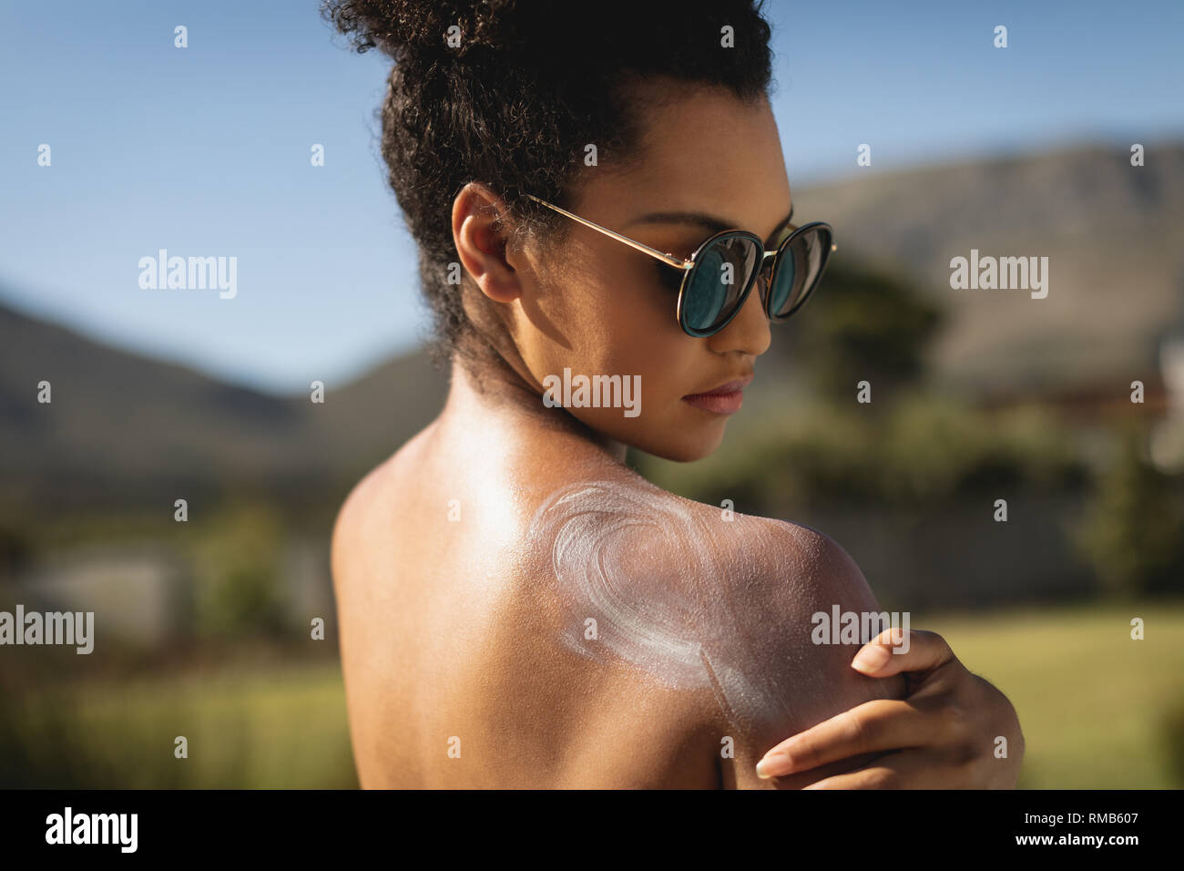 Young mixed-race woman rubbing sunscreen on shoulders Stock Photo