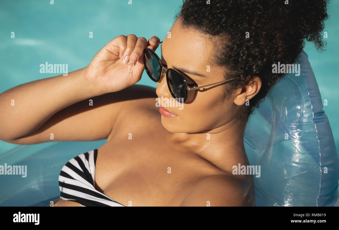 Young mixed-race woman with sunglasses relaxing on pool inflatable Stock Photo