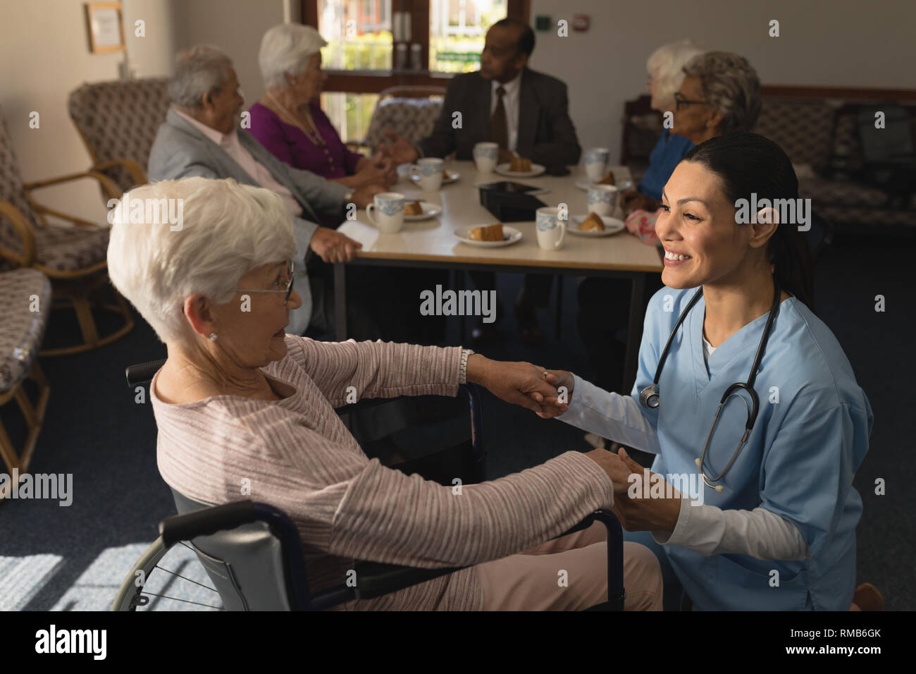 Side view of female doctor holding hands and talking with disable senior woman at nursing home Stock Photo