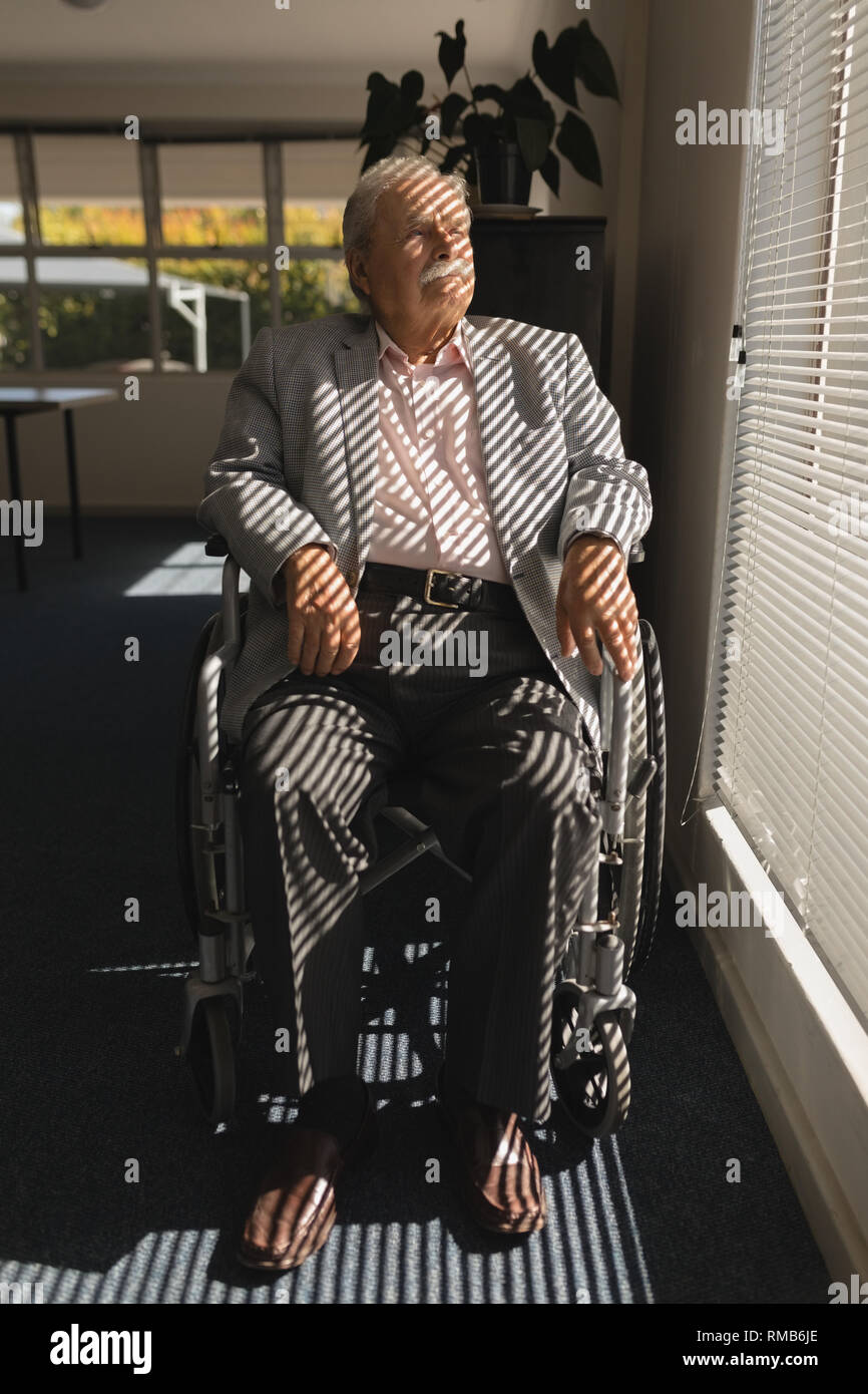 Front view of disable senior man sitting on wheelchair and looking outside through window Stock Photo