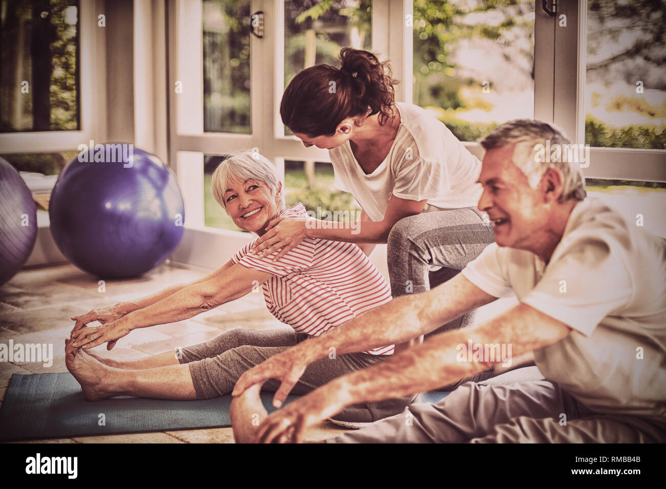 Female trainer assisting senior couple in performing exercise Stock Photo
