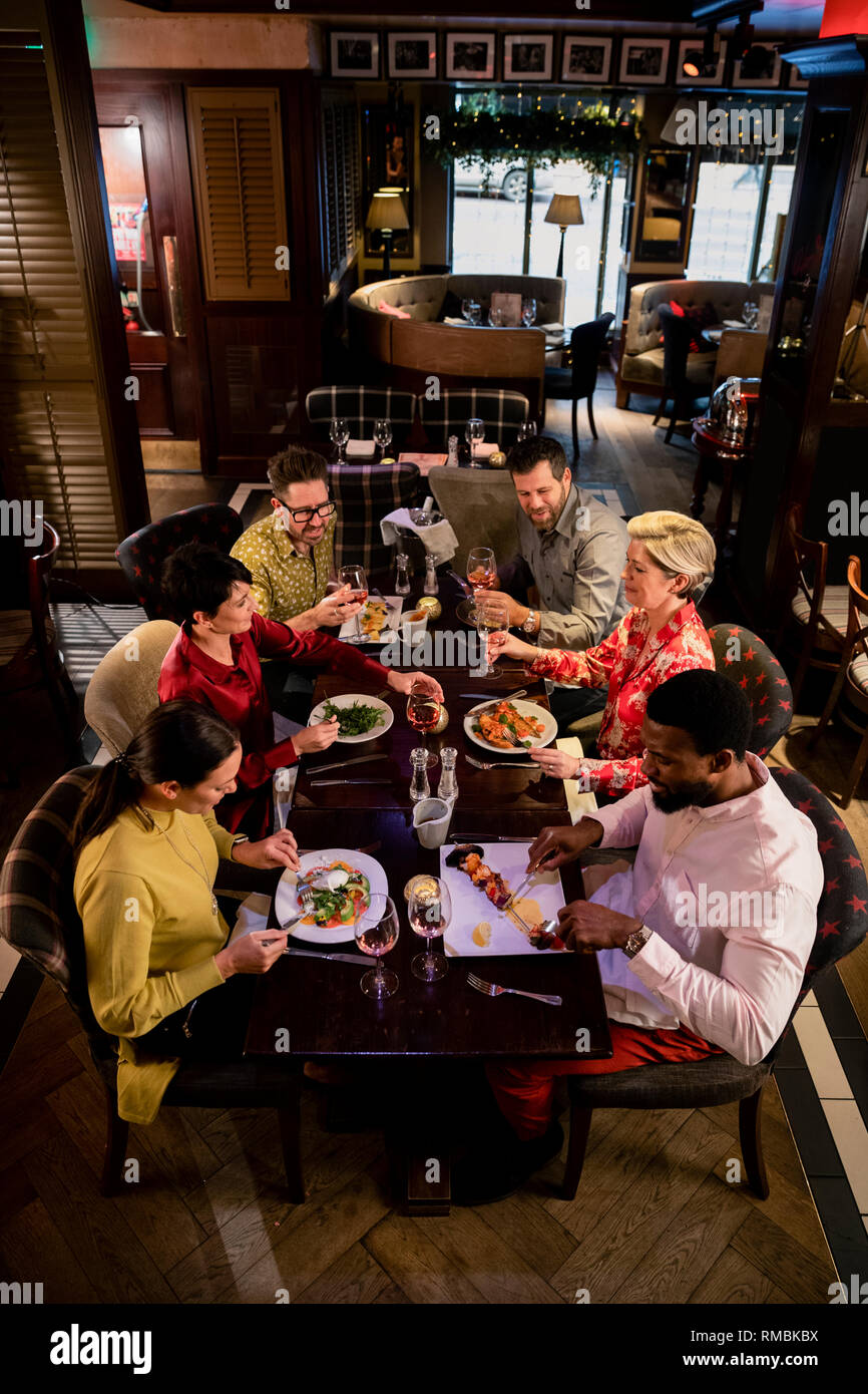 Small group of friends enjoying a meal in a restaurant. They are sitting at a table as they eat their food. Stock Photo