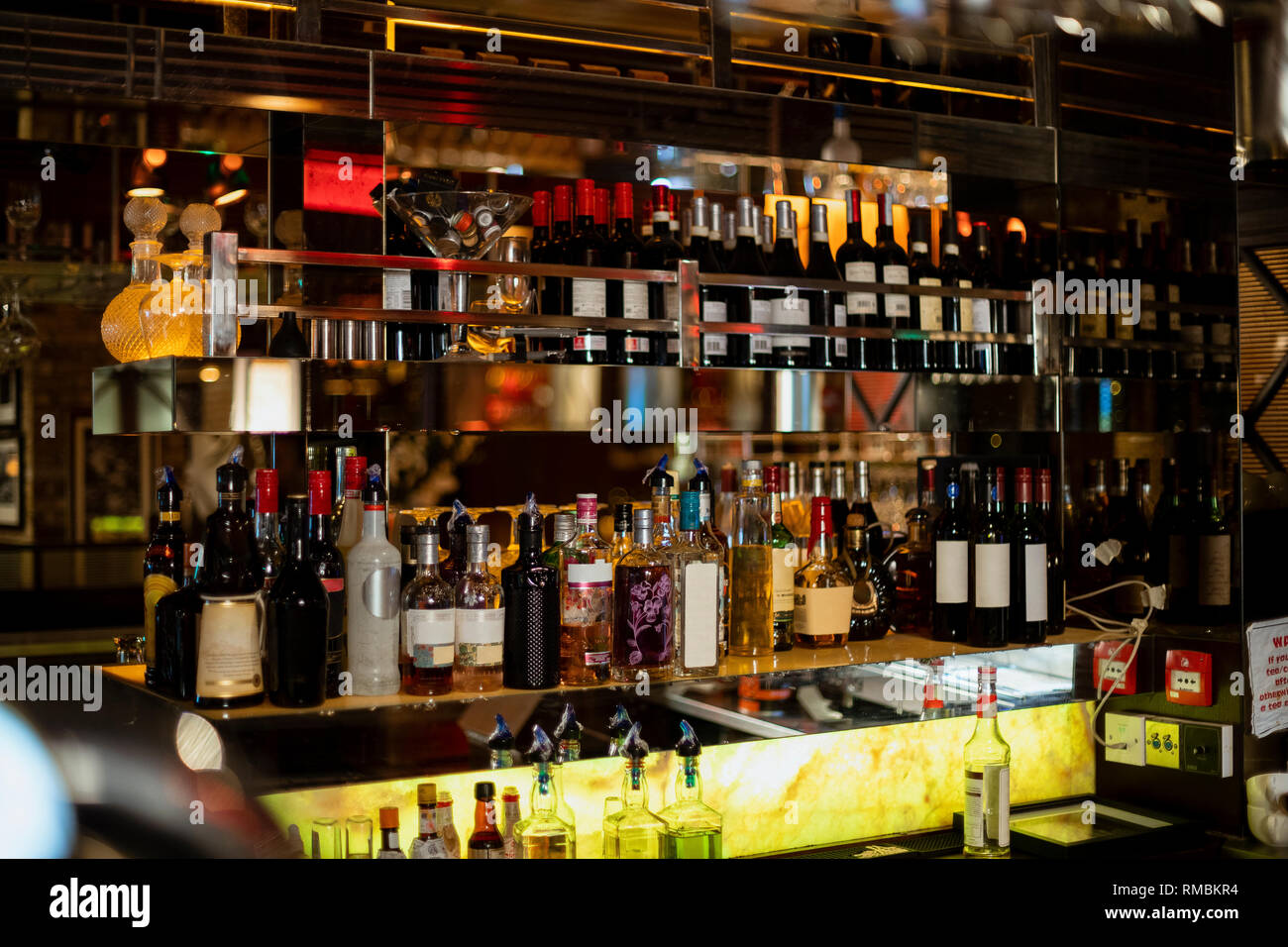 Front view of behind the bar counter in a restaurant. There are bottles of wine and various spirits on shelves. Stock Photo