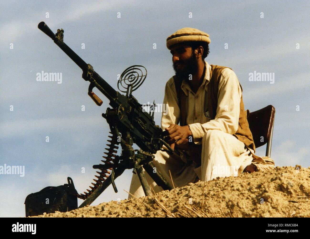 An Afghan fighter is guarding a warehouse on Pakistani territory with a heavy machine gun. The mujahedeen cross the border to rest in Pakistani camps and equip for the fight against Soviet troops. In the refugee camps further volunteers are being recruited. Stock Photo