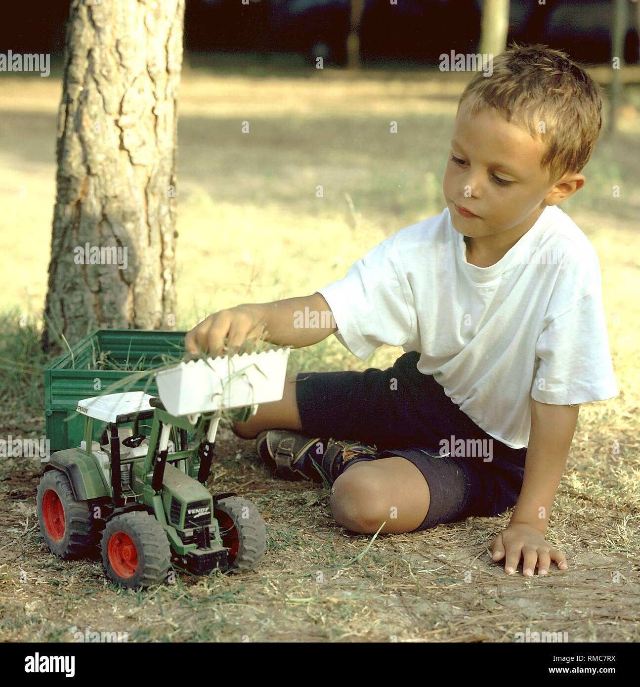 A little boy is playing outdoors with his toy tractor. Stock Photo
