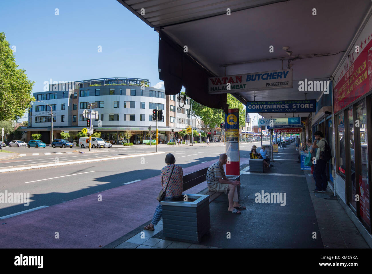 People wait at a bus stop near a set of traffic lights on Botany Road in the shopping area of the Sydney suburb of Mascot Stock Photo