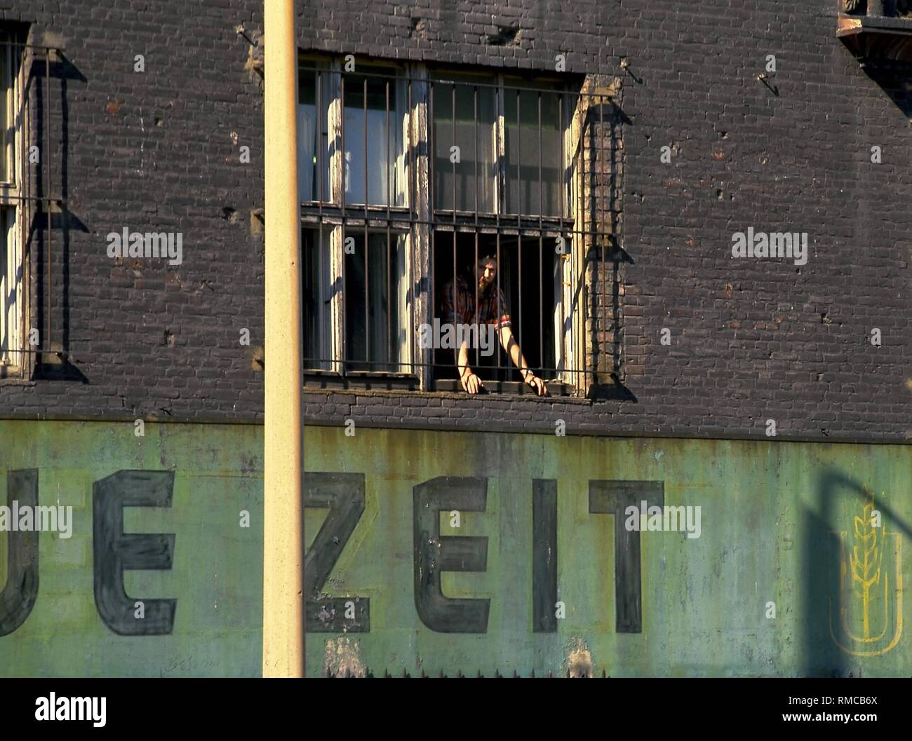 A worker peers through the barred window of the 'Neue Zeit' printing plant, the organ of the CDU in the GDR, in the Zimmerstrasse at the Berlin Wall. Stock Photo