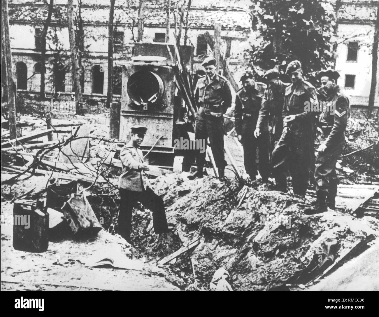 A soldier of the Red Army shows British soldiers the place, where the bodies of Eva Braun and Adolf Hitler were probably burned after their suicide in the garden of the Reich Chancellery. Stock Photo