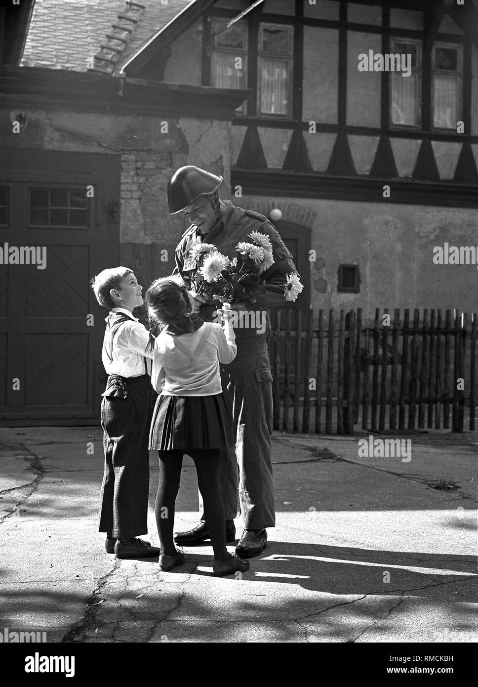 Two young pioneers present a bunch of flowers to an officer of the National People's Army (NVA). Stock Photo