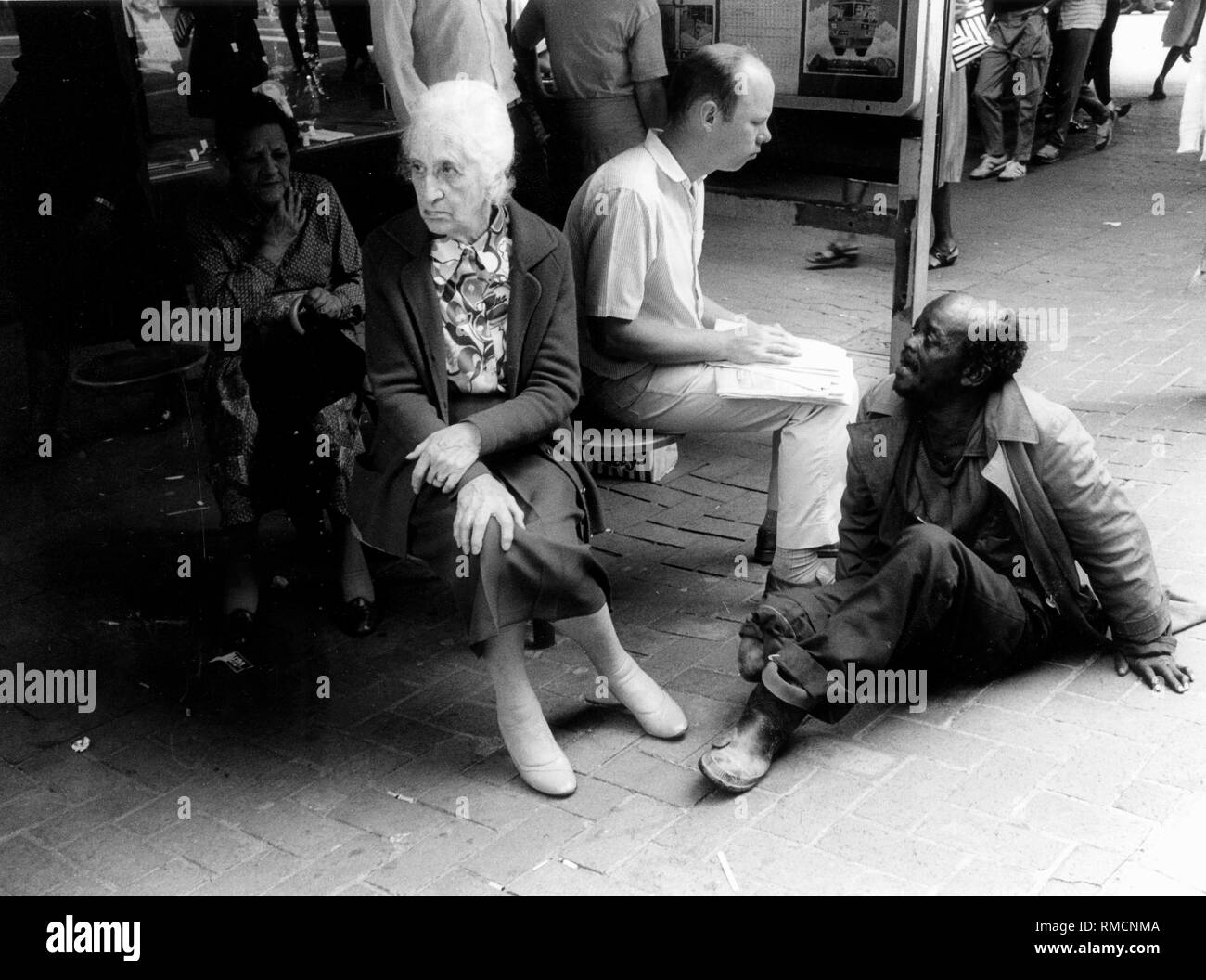 An old, crippled beggar in Johannesburg asks a white woman for alms. Stock Photo