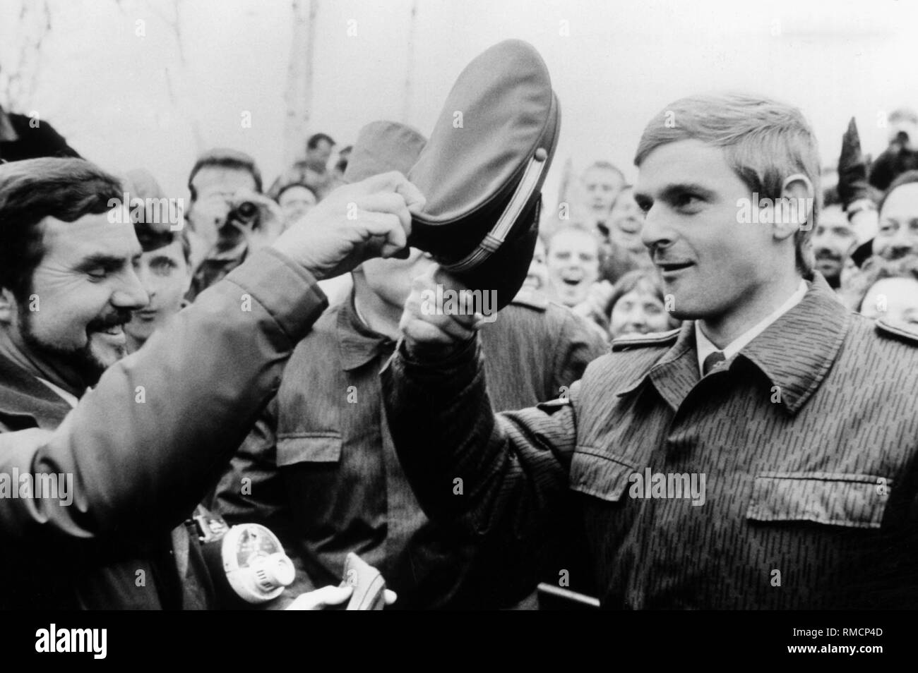 West Berlin policeman and East German Border Guard soldier in the crowd after the wall opening. The policeman hands his cap to the borderman. Stock Photo