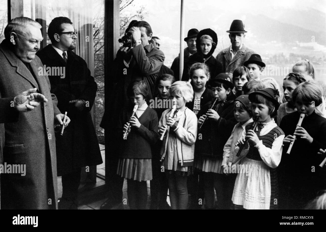 Children play a birthday serenade on the flute to Chancellor Ludwig Erhard (left) in front of his house in Gmund am Tegernsee. Stock Photo