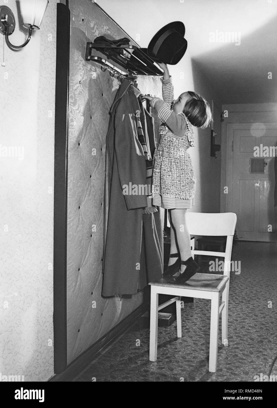 Girl puts a men's hat on the coatrack, 50s Stock Photo