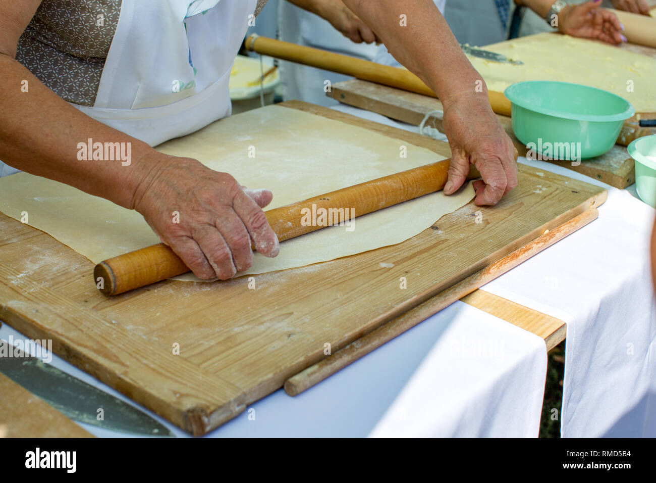 Old wrinkled hands of elderly woman rolling out dough with rolling pin on a wooden cutting board. Concept - benefits of cooking at home, active life i Stock Photo