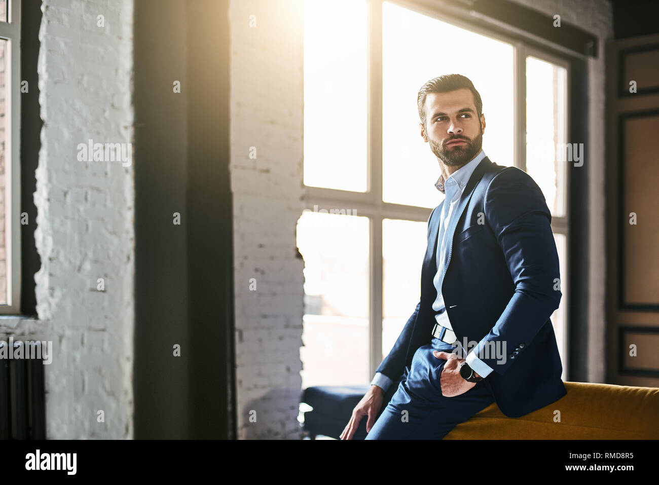 Fashion portrait. Young bearded successful businessman in stylish suit is standing at office and thinking about something. Fashon look. Business style Stock Photo