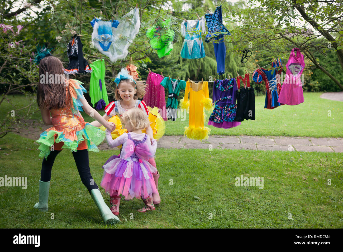 Three children dancing in a back yard surrounded by colourful washing on a clothes line. Stock Photo