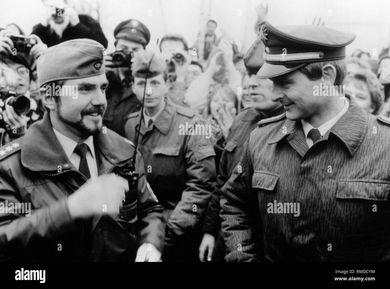 Berlin policemen together with GDR border guards after the fall of the Berlin Wall.  They changed hats and smile. In the background are photographers. Stock Photo