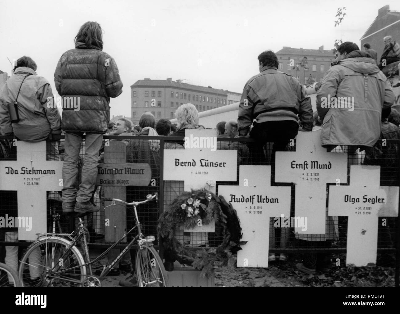Crosses commemorating the victims of the Berlin Wall, 1989.  Behind, a gathering of people shortly after the fall of the Berlin Wall at the crossing in Bernauerstrasse. On the crosses are the following names: Ida Siekmann, Bernd Luenser, Rudolf Urban, Ernst Mund, Olga Segler. Stock Photo