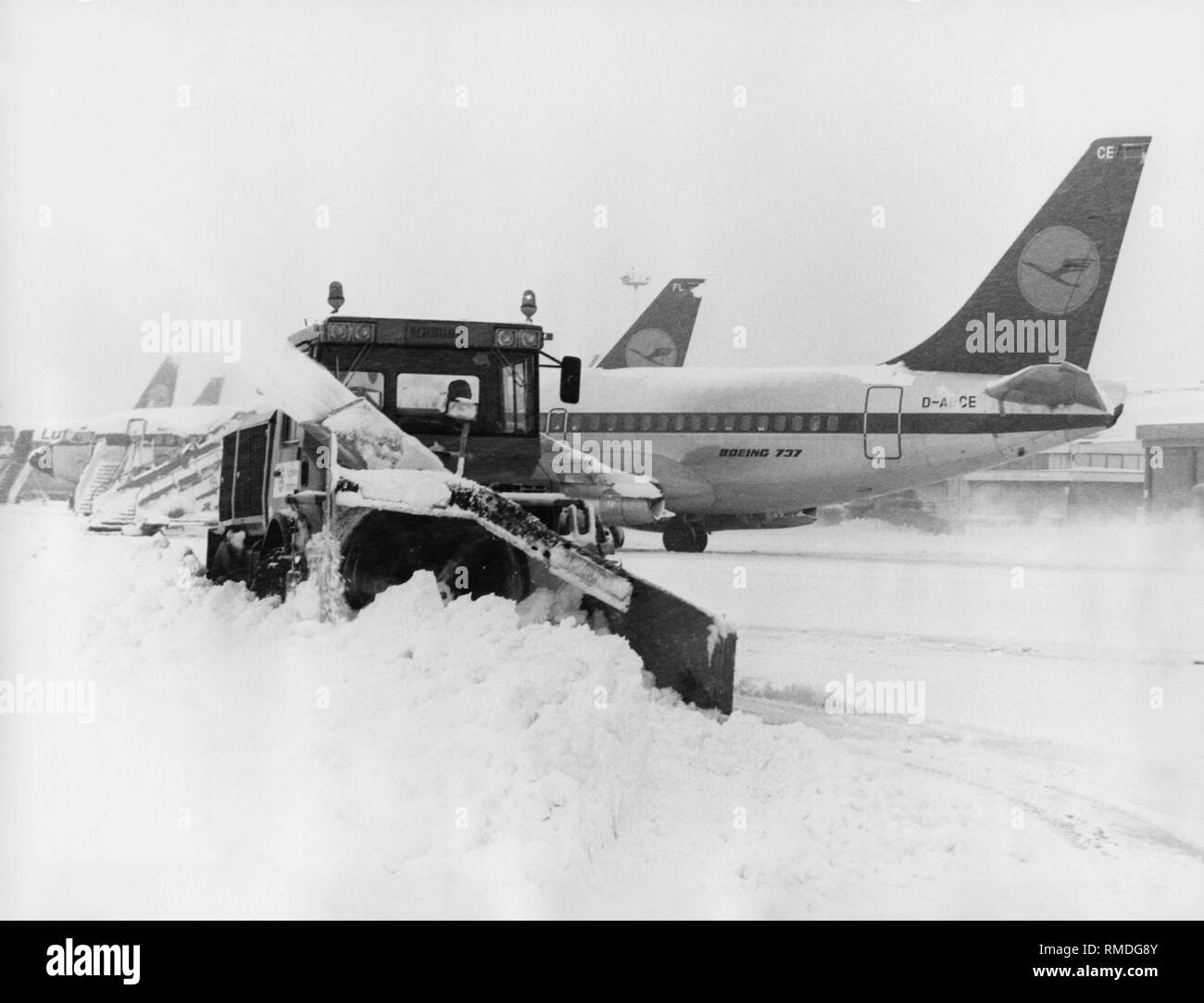 An apron is freed from the snow at Munich-Riem Airport. The aircraft in the background is the Lufthansa Boeing 737-200 with the registration D-ABCE and the name 'Landshut', which was abducted in October 1977. Stock Photo