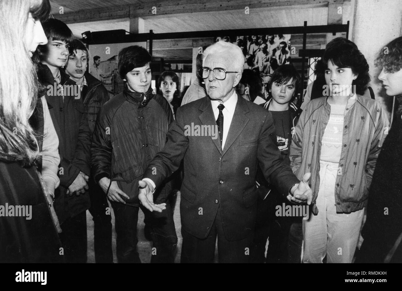 Adolf Meislinger, former concentration camp prisoner, leads young people presumably of the Aktion Suehnezeichen (Action Reconciliation) through the exhibition in the former agricultural building of the Dachau concentration camp, presumably in 1985. Stock Photo