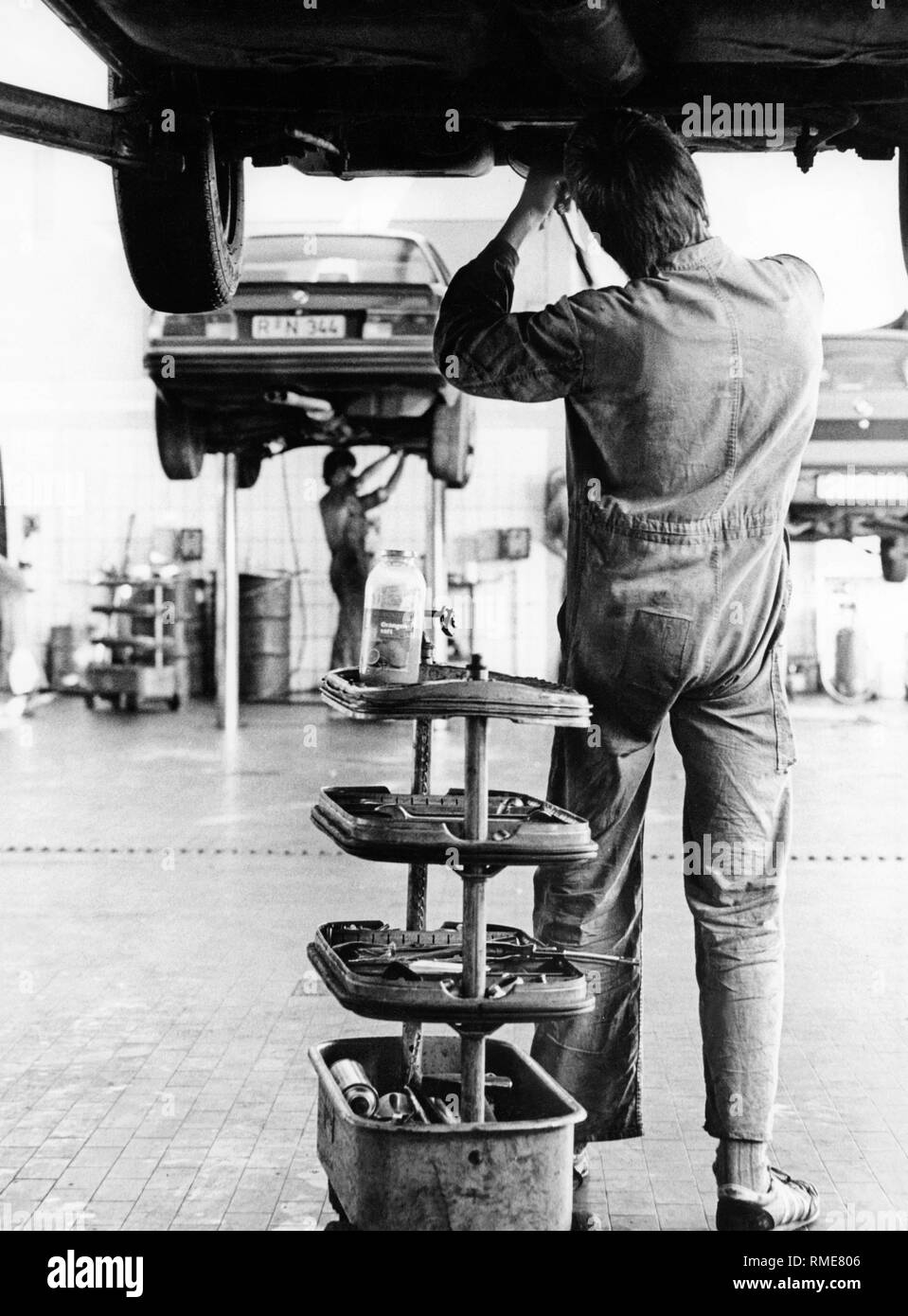 A car mechanic in a garage under a car on a service lift. On the left