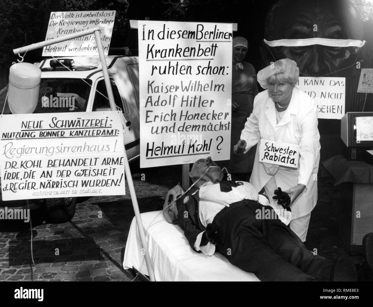 This photograph shows a demonstration against the moving of the government from Bonn to Berlin. Members of the Bonner-Buerger-Bund disguised themselves as doctors and nurses. This photograph shows a woman disguised as a nurse, 'Sister Rabiata,' who is treating a cabbage doll. On the protest posters are slogans such as 'New gossip: Use of the Bonn Chancellery: Government madhouse! Dr. Kohl treats poor lunatics, who were at the wisdom d. Government foolish! Assistant doctor Dr. Schaeuble.', 'The people are unemployed! The government is in the Berlin hospital and the state is broke! Stock Photo