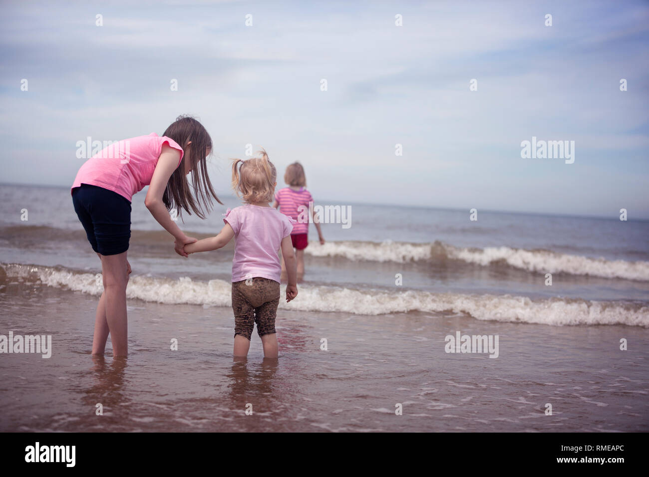 Three children paddling in small waves on the shore of the North Sea Stock Photo