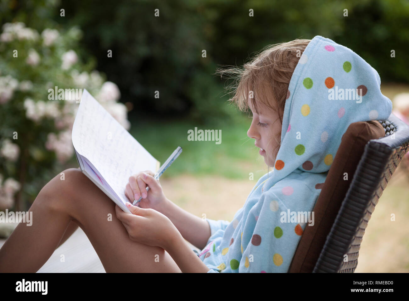 Child writing a letter whilst relaxing in a summer garden Stock Photo