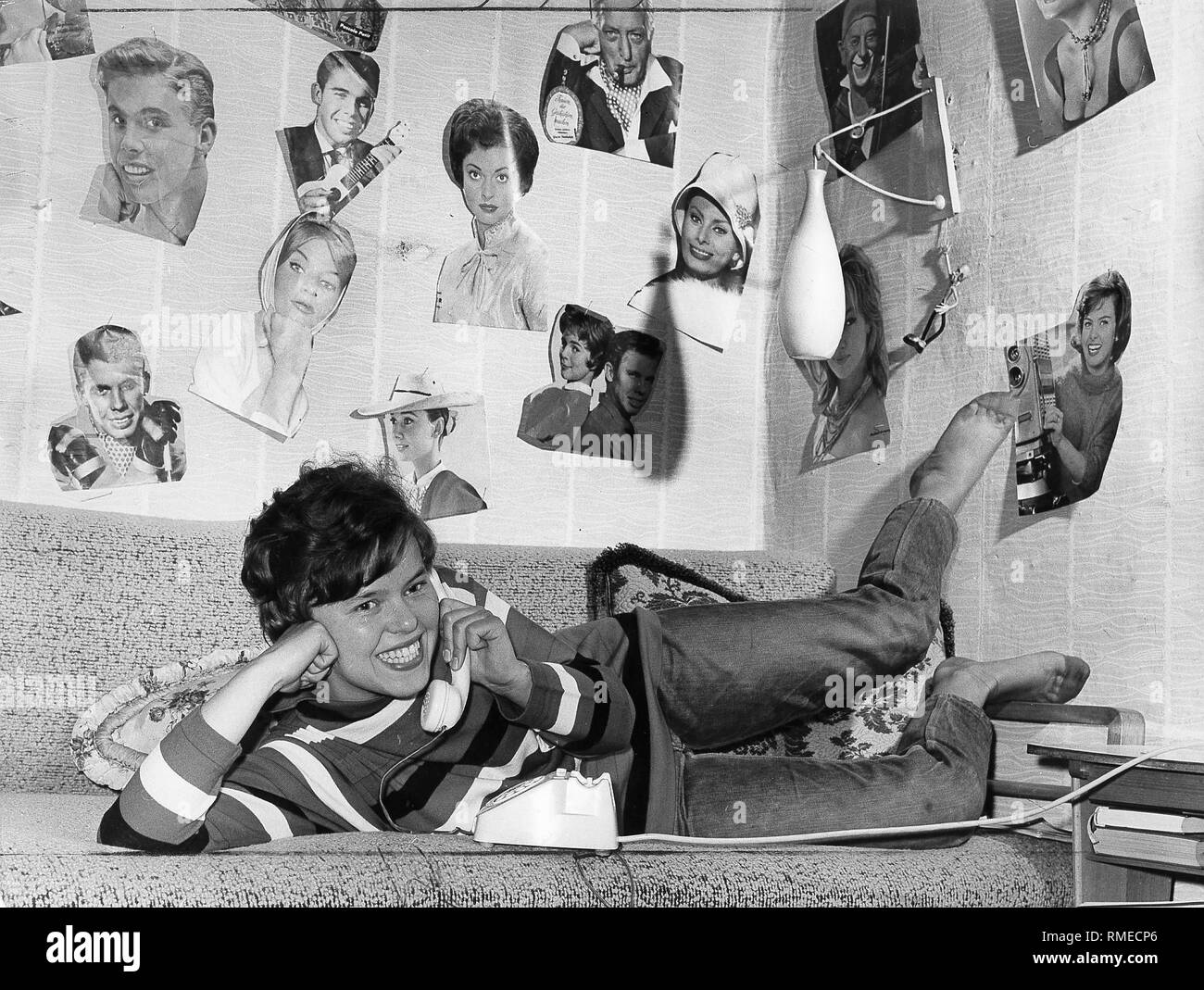 Young woman on the phone. On the wall are pictures by Hans Albers, Peter Kraus, Sophia Loren and Audrey Hepburn. Stock Photo