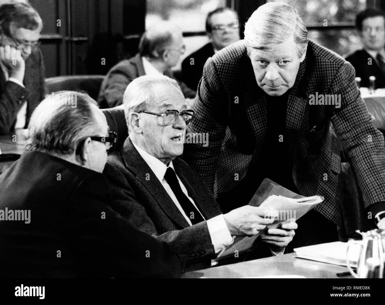 The group leader of the SPD Herbert Wehner (center) talking with Chancellor Helmut Schmidt (right) and the deputy party chairman Hans-Juergen Wischnewski (left) in the Bundestag. In the background are further deputies. Stock Photo